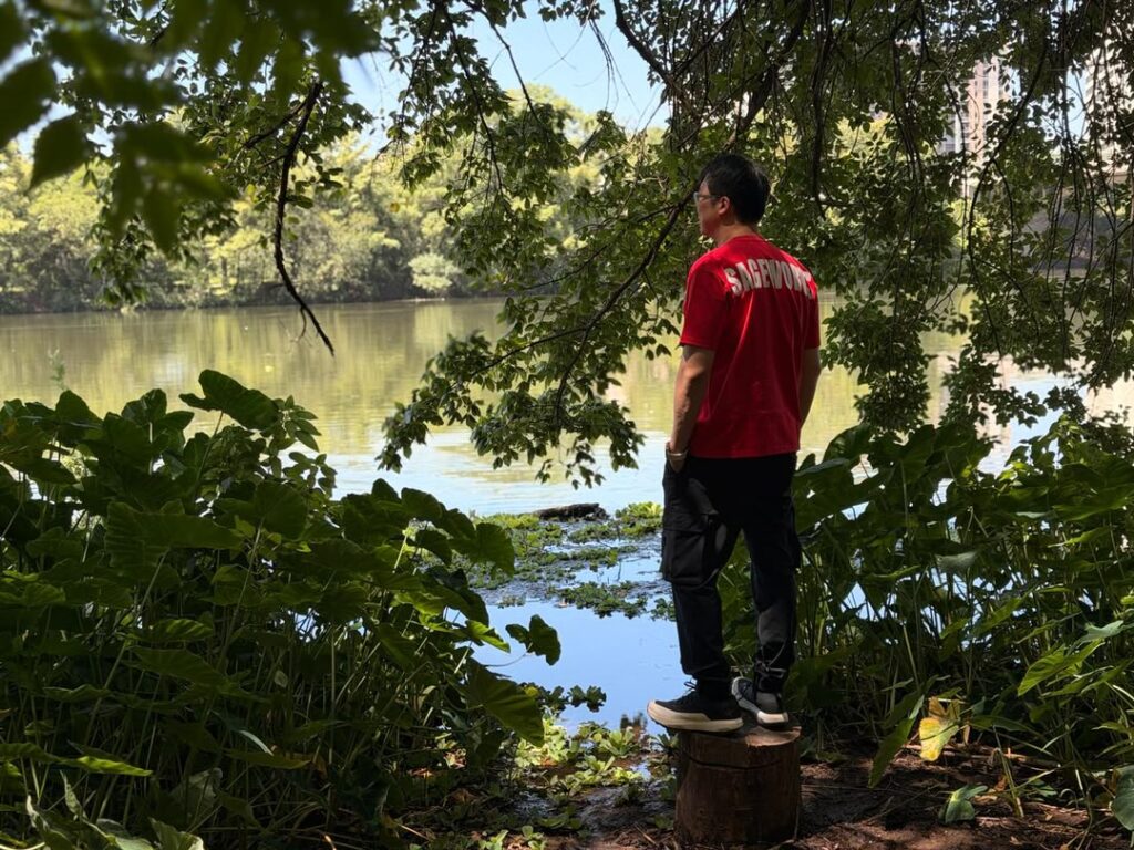 Joey Yap standing on a tree stump overlooking the still water of Austin's dammed lake, framed by overhanging trees